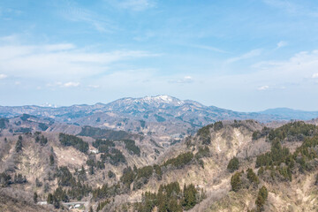雪解け直後の山肌が見える春の山々を空撮したドローン風景