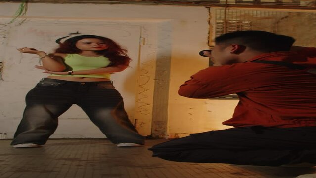 Vertical shot of man taking photos of Asian woman against shabby graffitied wall indoors