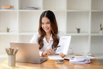A young, smiling businesswoman confidently engages in a video conference call on her laptop in a modern office.