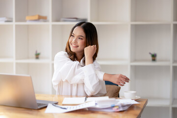 A relaxed businesswoman stretch and relieve tension while working at her desk in a bright office.