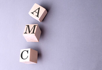 AMC word on wooden block on gray background