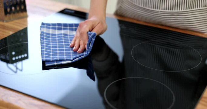 Housewife wiping glass surface of induction cooker with towel closeup 4k movie slow motion. Home appliance care concept 