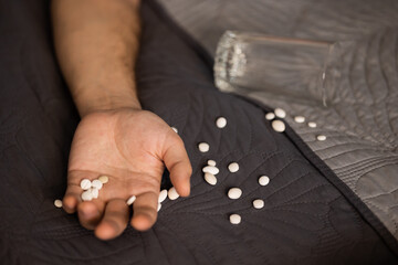 Hand, white pills, glass of water. Man lying bed. suicide attempt sleeping pills and...