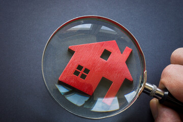 Property valuation. A figurine of a house and a hand with a magnifying glass.