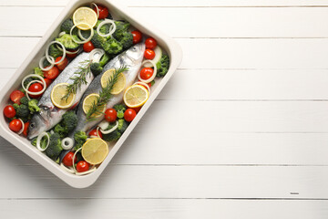Raw fish with vegetables and lemon in baking dish on white wooden table, top view. Space for text