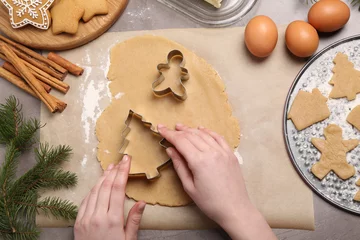 Tuinposter Woman making Christmas cookies with cutters at grey table, top view © New Africa