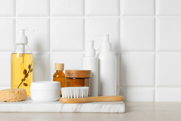 Different bath accessories and personal care products on wooden table near white tiled wall