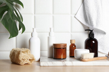 Different bath accessories and personal care products on wooden table near white tiled wall
