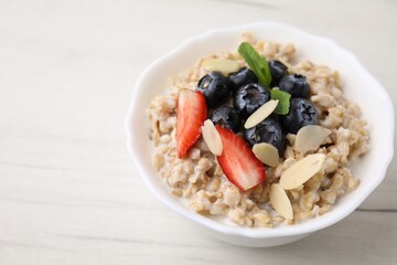 Tasty oatmeal with strawberries, blueberries and almond petals in bowl on white wooden table, closeup. Space for text