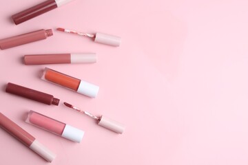 Different lip glosses and applicators on pink background, flat lay. Space for text