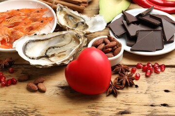 Natural aphrodisiac. Different food products and heart model on wooden table, closeup