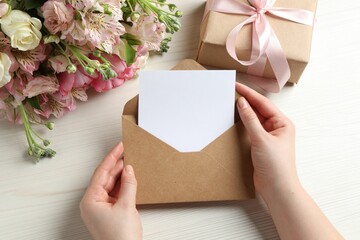 Happy Mother's Day. Woman holding envelope with blank card at white wooden table, top view - obrazy, fototapety, plakaty