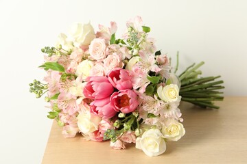 Beautiful bouquet of fresh flowers on wooden table near light wall