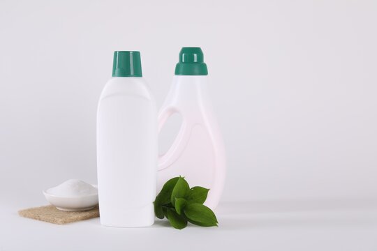 Bottles of cleaning product, baking soda and green leaves on white background