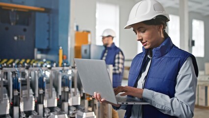 Close-up portrait of beautiful middle-aged female engineer looking watching at product making process. Woman nodding and putting information into her big grey gadget.