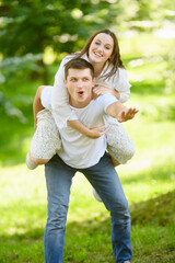 Young happy couple in love resting in nature. Woman jumped on man back, he spins her around, having...