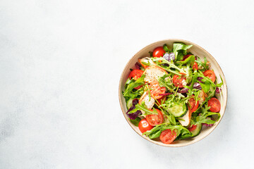 Green salad with baked chicken breast, fresh salad leaves and vegetables. Top view on white background.