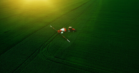 Tractor spraying pesticides on wheat field with sprayer in spring.	