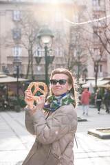 Beautiful young woman having fun with bagel outdoor on the street