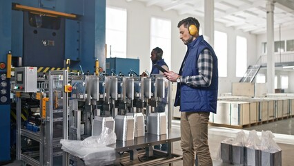 Handsome attractive good-looking charming tall middle-aged Caucasian man in professional headphones doing usual routine tasks. Worker carefully wrapping up machinery product.