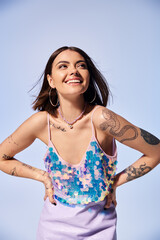 Brunette woman confidently stands with hands on hips, flaunting tattoos in studio setting.