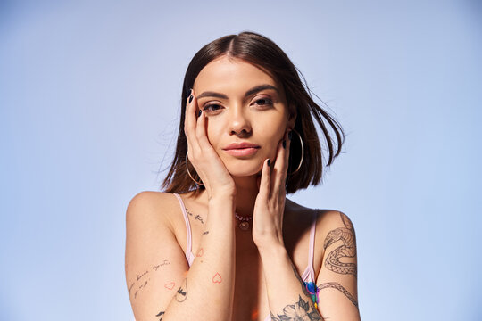 A young woman with brunette hair proudly displays a tattoo on her arm while striking a pose in a studio setting.