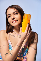 A brunette woman with tattoos holding a bottle of sunscreen.