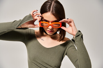 Brunette woman in a vibrant green shirt and trendy orange glasses poses confidently in a studio...