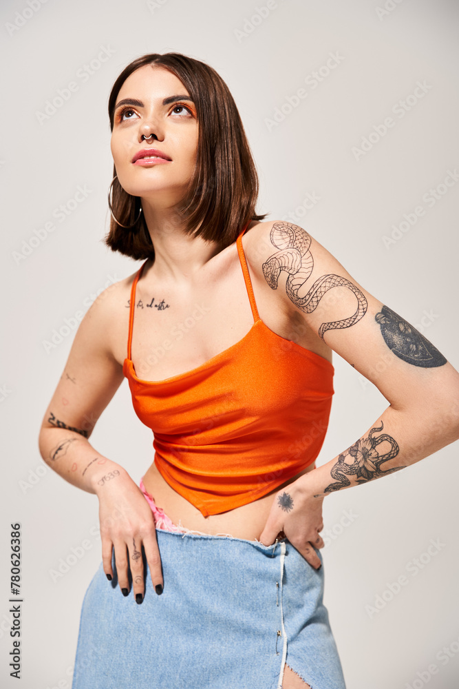 Canvas Prints A young woman with brunette hair striking a confident pose, hands on hips, in a vibrant orange top in a studio setting.