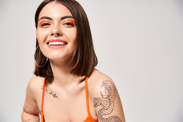 A stylish young woman with brunette hair displaying a beautiful tattoo on her arm in a studio setting.