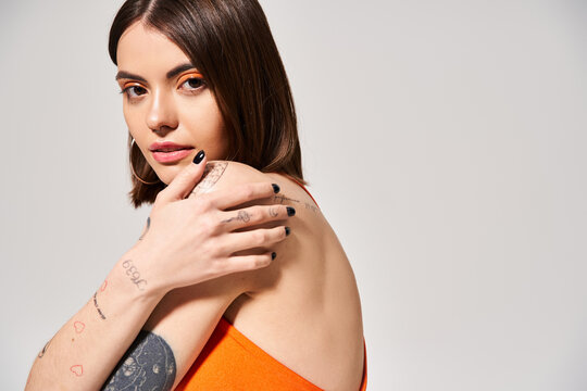 A young woman with brunette hair showcasing a tattoo on her arm in a studio setting.