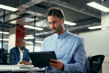 Fototapeta na wymiar Two multiracial men in businesswear using digital tablet during meeting in office