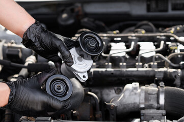 Replacing auto parts in a car. Repairman black gloves holds bypass and parasitic rollers against...
