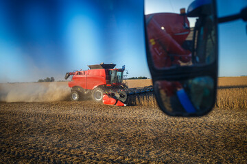 A combine harvester at work seen from inside a tractor while harvesting a soybean field.