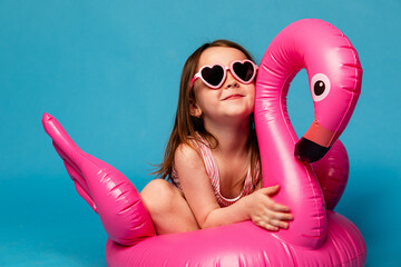 Happy child girl in pink swimsuit with swimming ring flamingo on a colored blue background. Travel,...