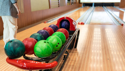 Bowling player contemplating over assorted colorful bowling balls on alley rack.