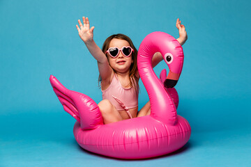 Happy child girl in pink swimsuit with swimming ring flamingo on a colored blue background. Travel,...