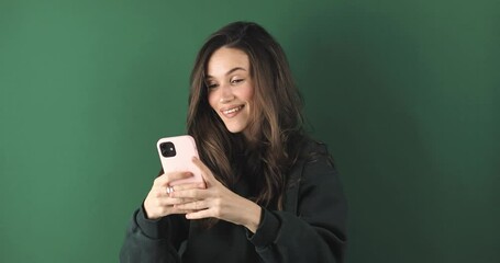Happy young casual woman in green pullover reading and scrolling social media look happy, point like or dislike say wow standing isolated green background.