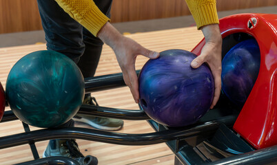 Person selecting colorful bowling balls from the rack at a bowling alley.