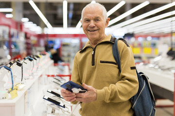 Elderly grayhaired man pensioner examining counter with electronic gadgets and tablets in showroom of digital goods store