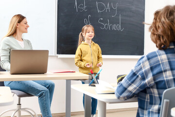 Little smiling girl standing near green blackboard in classroom. Education concept. Back to school