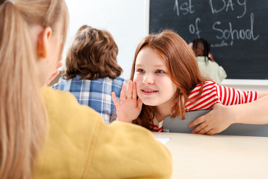 Small girl telling secret to other girl in school during lesson. Education concept. Back to school