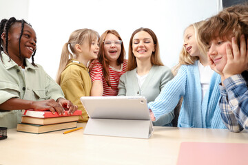 Kids laughing while standing near teacher, using digital tablet on the lesson. Education, learning