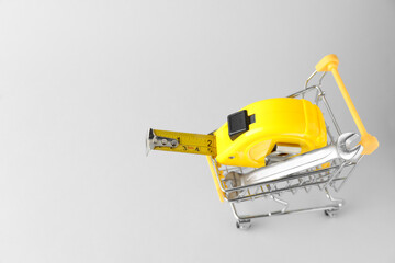 Naklejka premium Metal wrench and measuring tape in shopping cart on light grey background, above view. Space for text