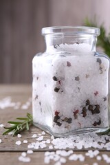 Salt with peppercorns in glass jar and rosemary on wooden table, closeup