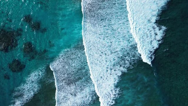 Aerial top view of incredibly powerful and towering white waves crashing against barrier reef in Caribbean Sea. This abstract spectacle unfolds before us from bird's-eye view. Zoom in