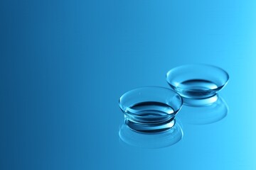 Pair of contact lenses on mirror surface, toned in blue. Space for text