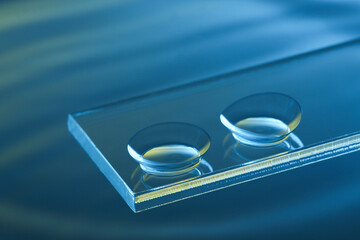 Pair of contact lenses on glass against blue background, closeup