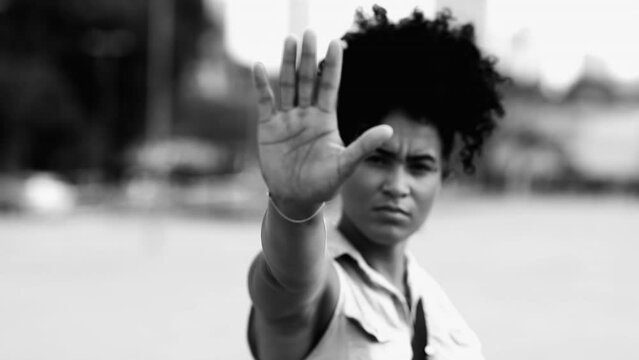 Young woman saying STOP with hand gesture. Person of African Descent showing hand rejecting offer with stern serious expression in black and white