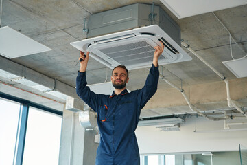 A man repairs the ventilation system, the device hangs on the ceiling